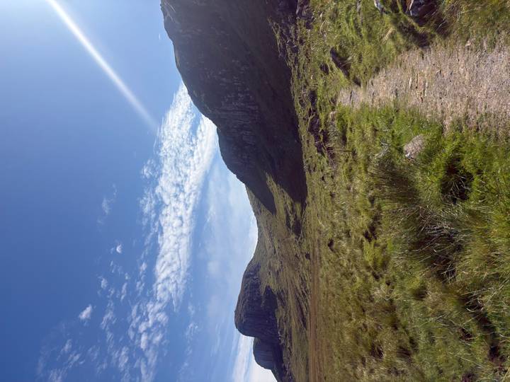 Sunny Highland valley with grassy path leading between rolling hills under a crisp blue sky.