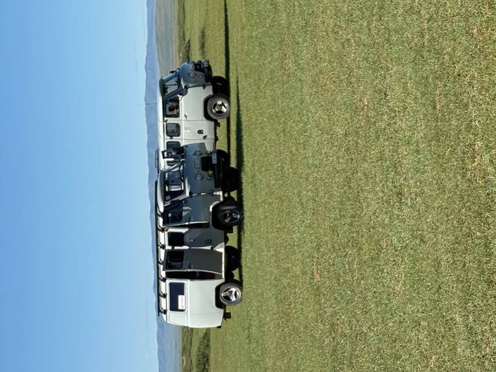 Row of classic Soviet UAZ vans parked on open grassland beneath a clear blue sky.