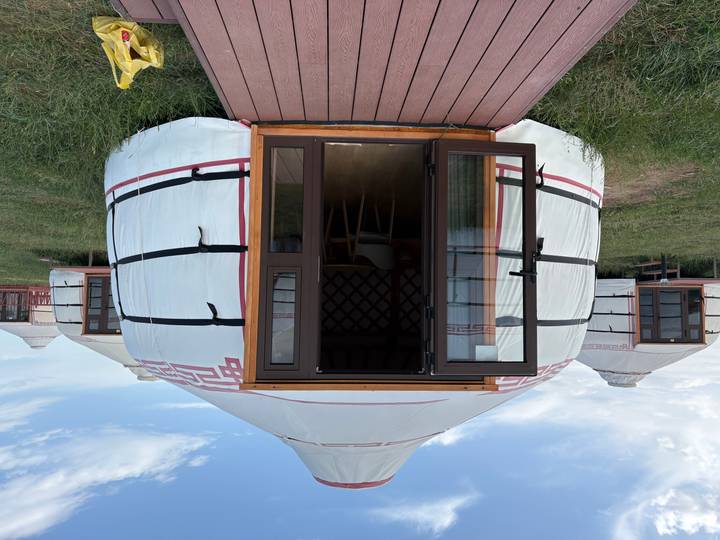 Modern ger with open door and wooden deck set on a grassy steppe, with similar yurts in the background.