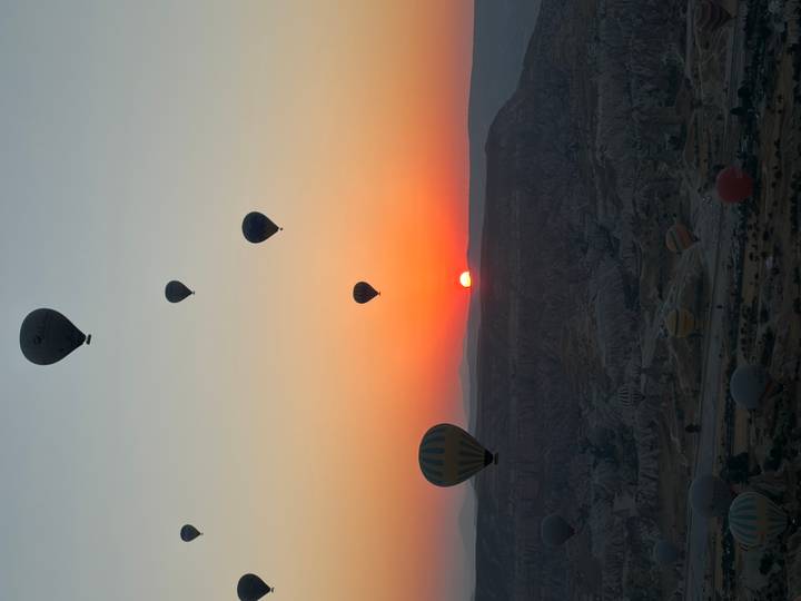 Silhouetted hot-air balloons ascending into a vivid orange sunrise above the rocky valleys of Cappadocia.