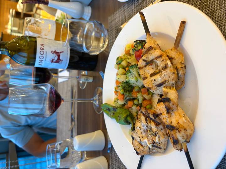 Grilled chicken skewers with mixed vegetables, wine and beer on a restaurant table.