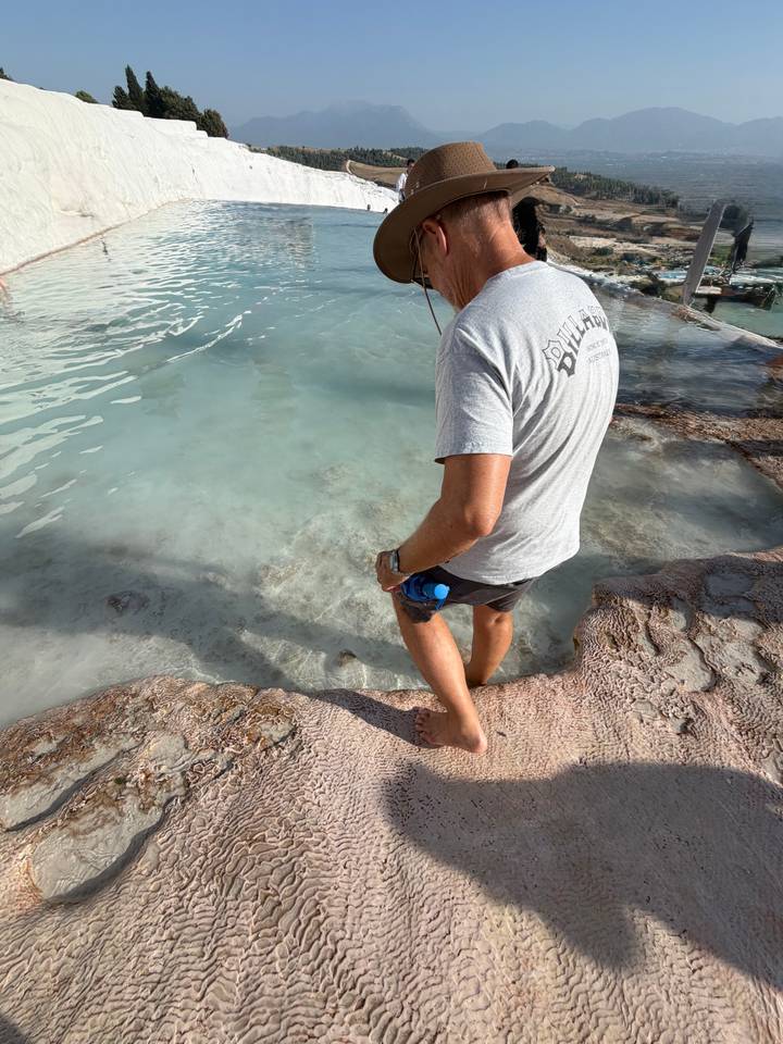 Visitor dipping feet into pale turquoise thermal water along the travertine terraces of Pamukkale.