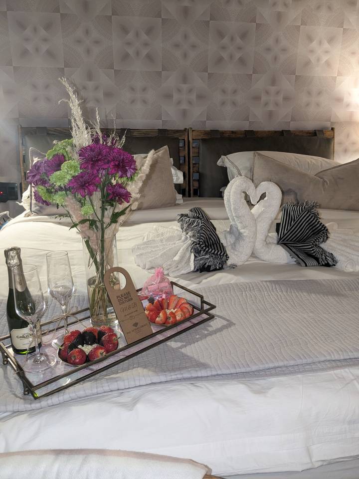 Luxurious hotel bed decorated with towel swans, flowers, champagne and strawberries on a tray.