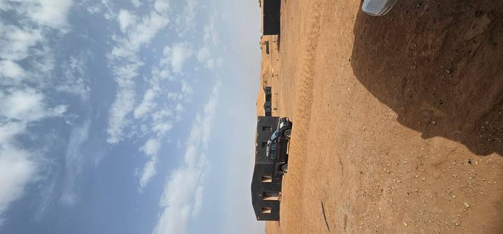 Remote desert camp with black canvas huts and a pickup truck beneath scattered clouds.