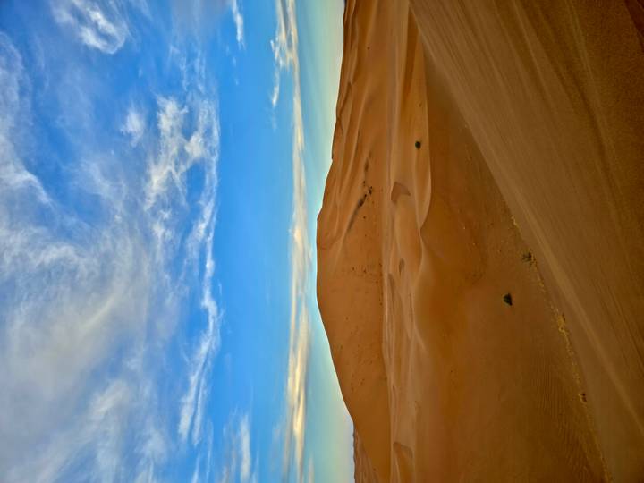Vast orange dunes under blue sky streaked with wispy clouds at dusk.