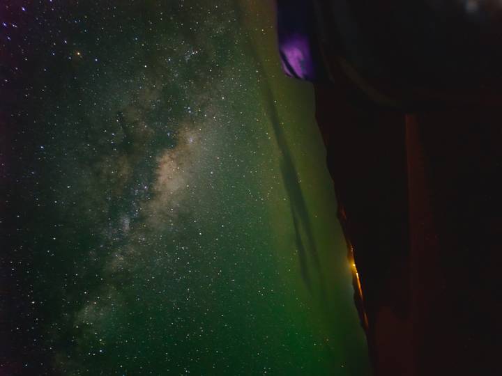 Star-filled sky above silhouetted dunes with faint glow of distant lights on horizon.