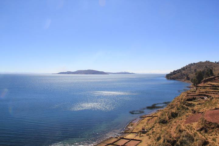 Wide serene view of a deep blue lake with distant islands beneath a clear sky.