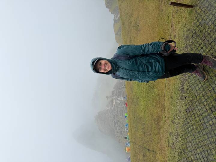 Smiling hiker in rain jacket stands before fog-shrouded ruins of Machu Picchu.