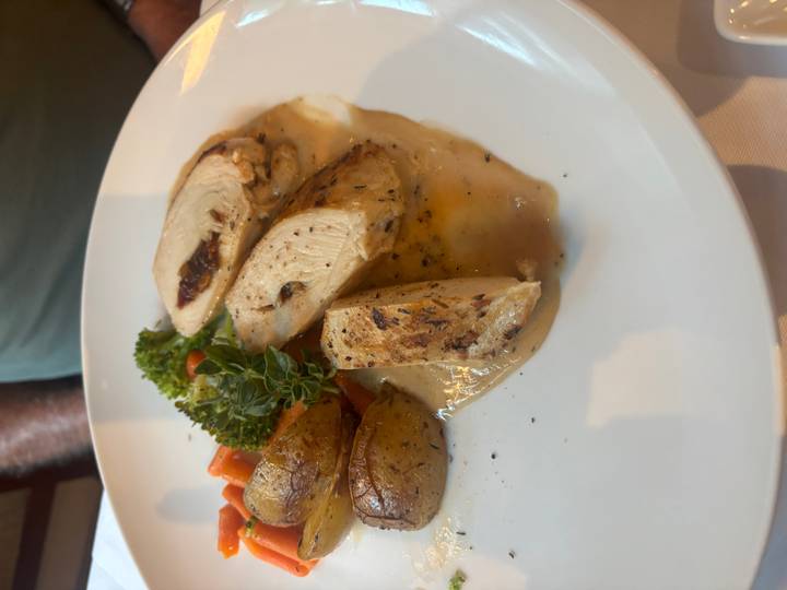 Plated main course of roasted chicken breast with potatoes, vegetables and herb garnish.