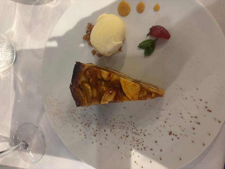 Slice of apple tart served with vanilla ice-cream, strawberry and mint on a white plate.