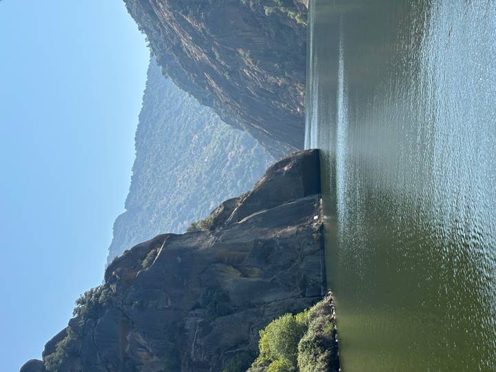 Serene river gorge bordered by tall rocky cliffs and forested mountains under a clear sky.