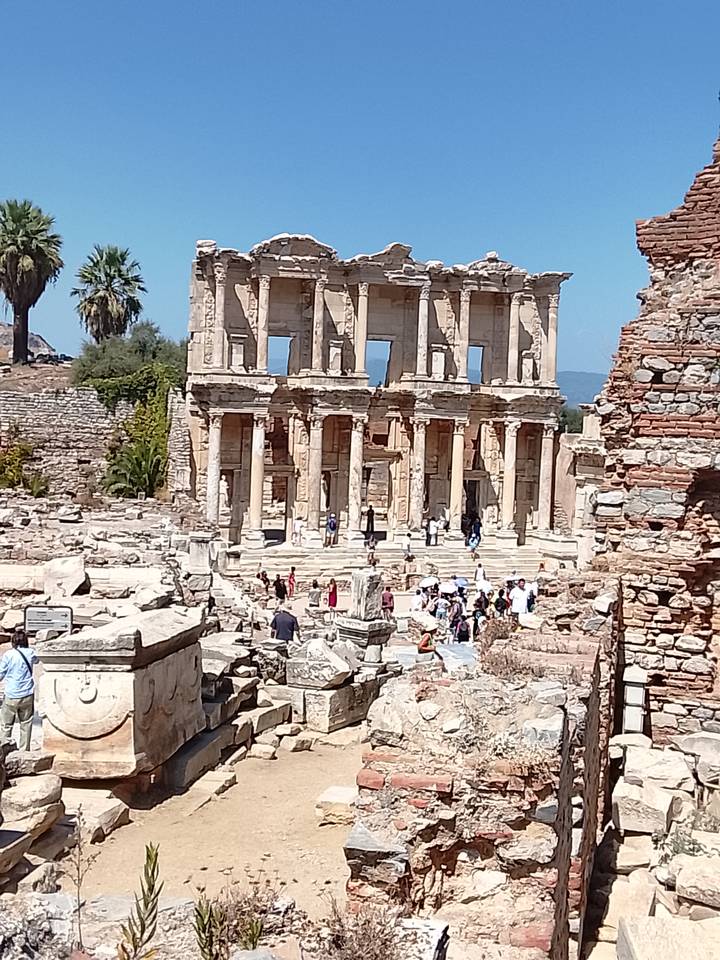 Ancient stone façade of the Library of Celsus with tourists exploring the surrounding ruins.