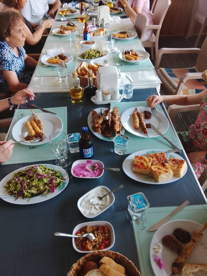 Tabletop view of Turkish meal with skewers, salad, meze and Efes beer as diners reach for food.