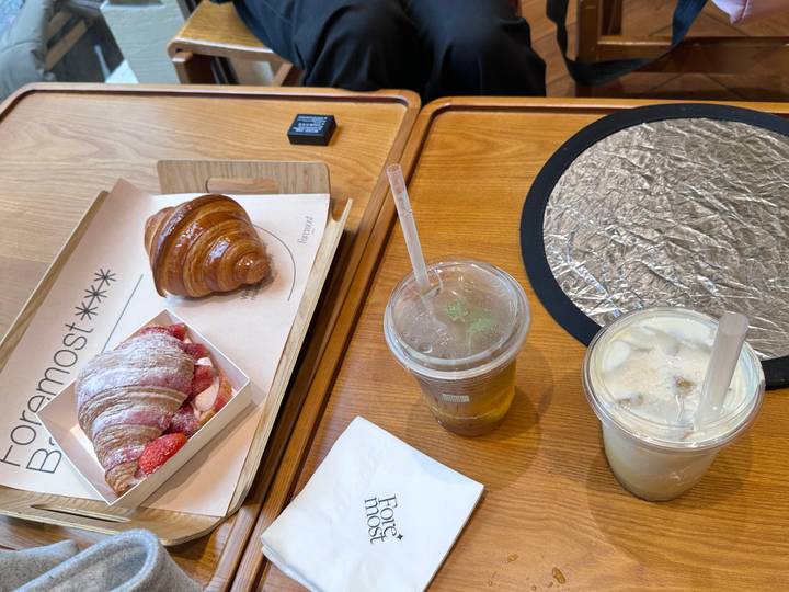 Wooden café table set with croissant, strawberry pastry and two iced drinks.