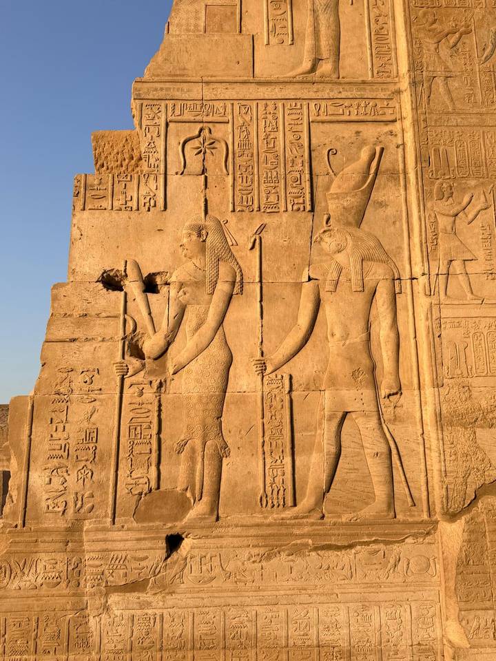 Sunlit sandstone reliefs depicting ancient Egyptian deities and hieroglyphics on a temple wall.