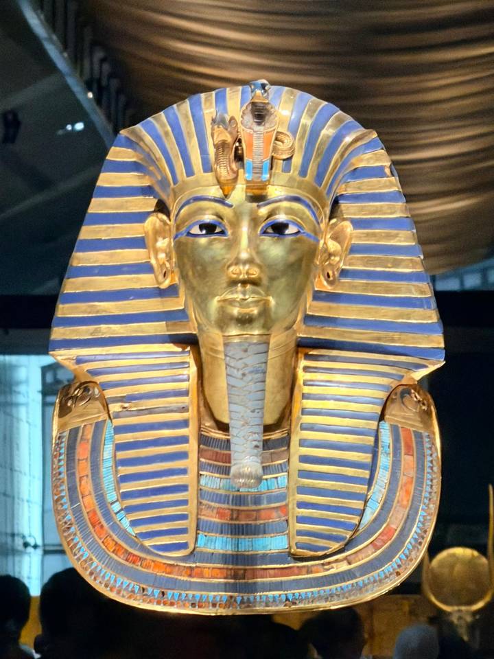 Close-up of the gleaming golden funerary mask of Tutankhamun displayed in a museum case.