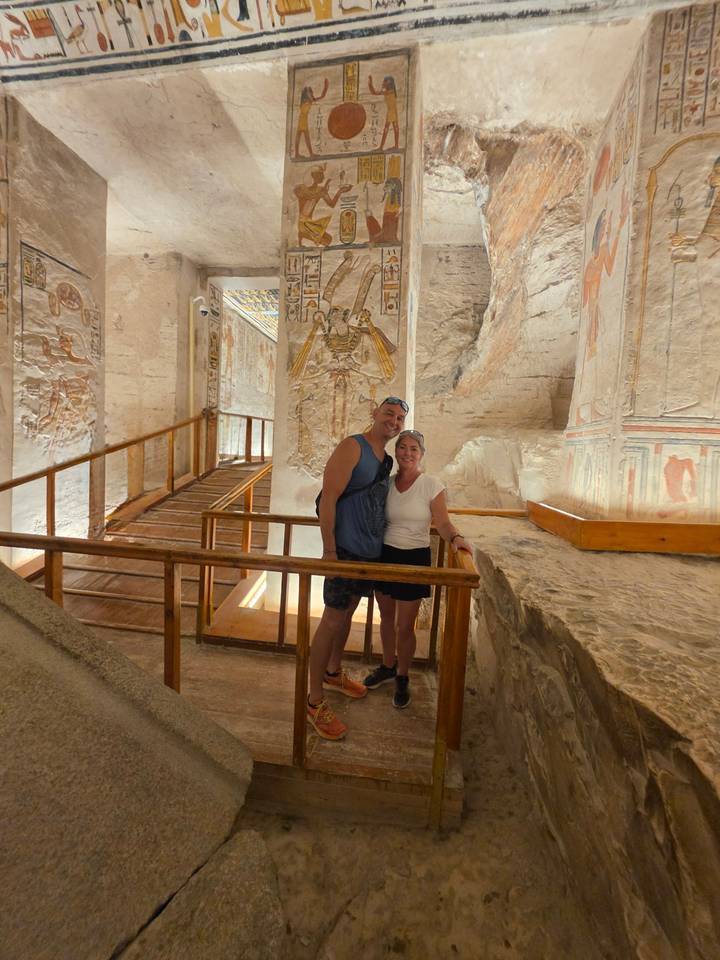 Travelers stand inside an ancient Egyptian temple hallway adorned with colorful reliefs and wooden walkways.