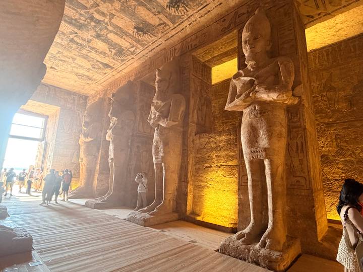 Tourists explore a hall lined with towering carved statues bathed in warm interior lighting.