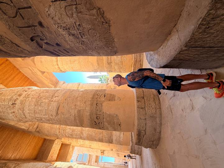 Traveler gazes upward at monumental hieroglyph-covered columns inside an ancient hall.