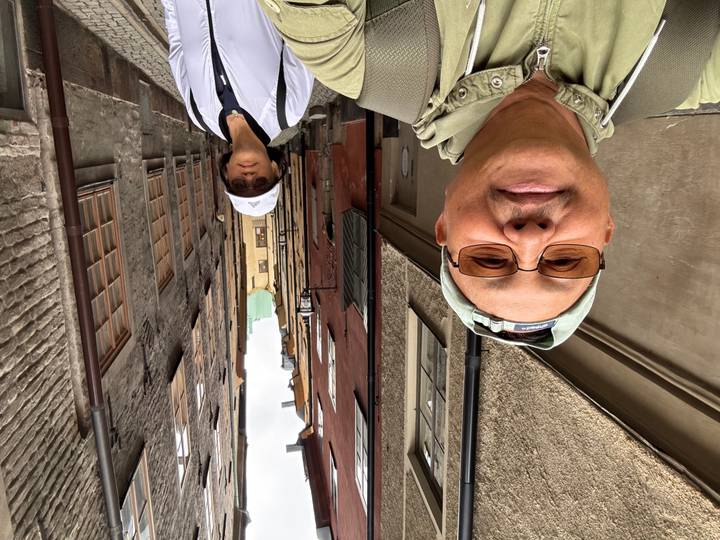 Selfie of couple standing in narrow cobblestone alley lined with colorful medieval facades of Stockholm’s Gamla Stan.