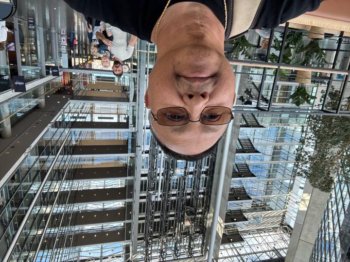 Man’s selfie inside modern glass atrium filled with steel beams, elevators and reflective surfaces.