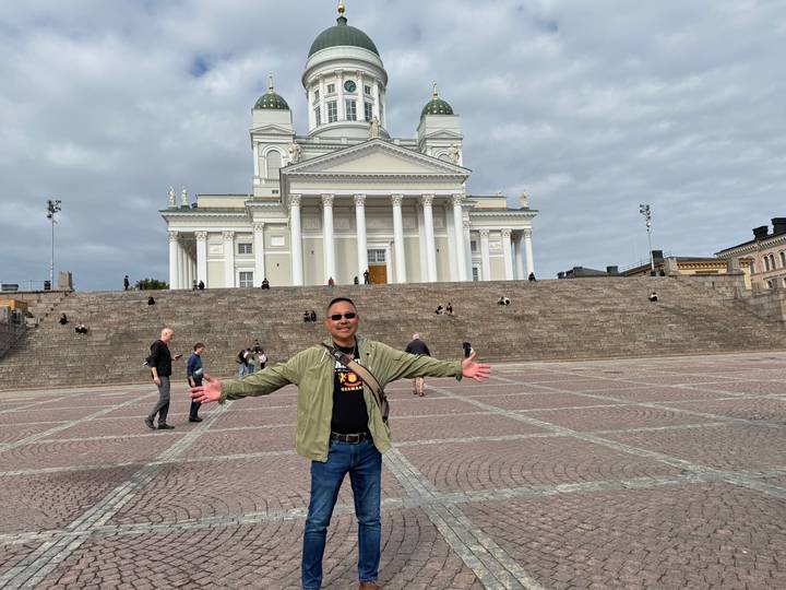 Man spreads arms joyfully in front of Helsinki Cathedral on spacious Senate Square.