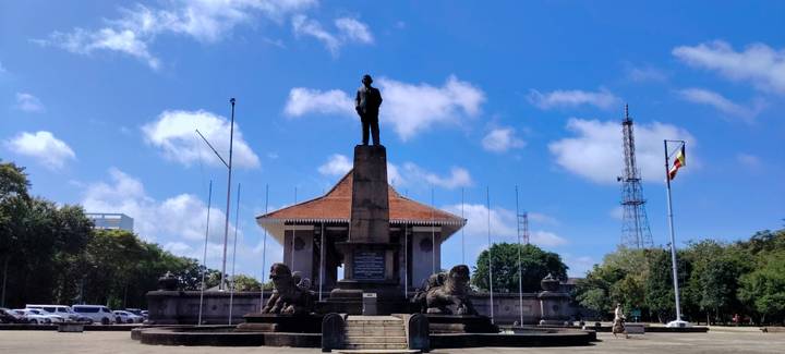 Statue-topped monument flanked by stone lions and flagpoles at Independence Square in Colombo under a bright sky.
