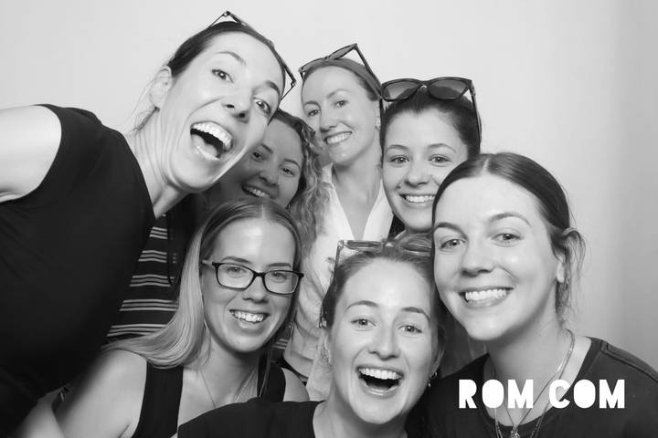 Black-and-white photo-booth style portrait of seven friends smiling inside a studio setting with overlay text in the corner.