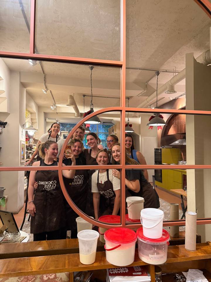 Cooking class participants posing happily behind a counter filled with kitchen utensils.