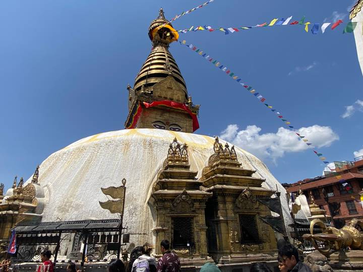 Golden stupa with the iconic Buddha eyes and prayer flags streaming into a clear blue sky.