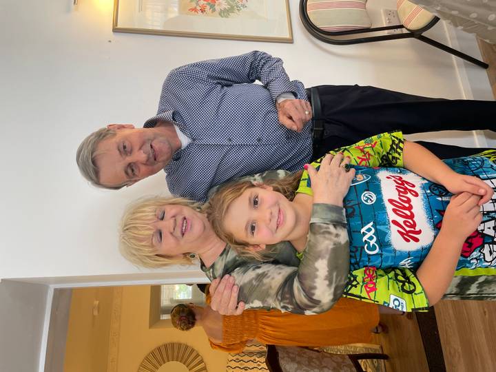 Smiling grandparents hug their granddaughter inside a bright home.