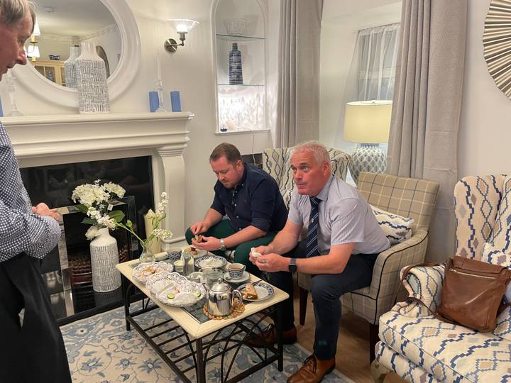 Two men enjoy afternoon tea with fine china and pastries in an elegant lounge.