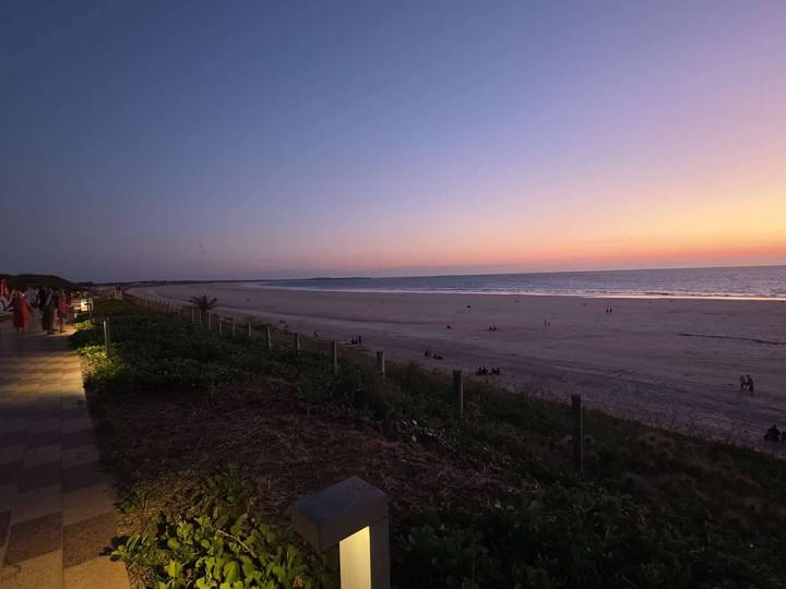 Wide sunset view of an expansive empty beach and gentle sea with pastel sky hues.