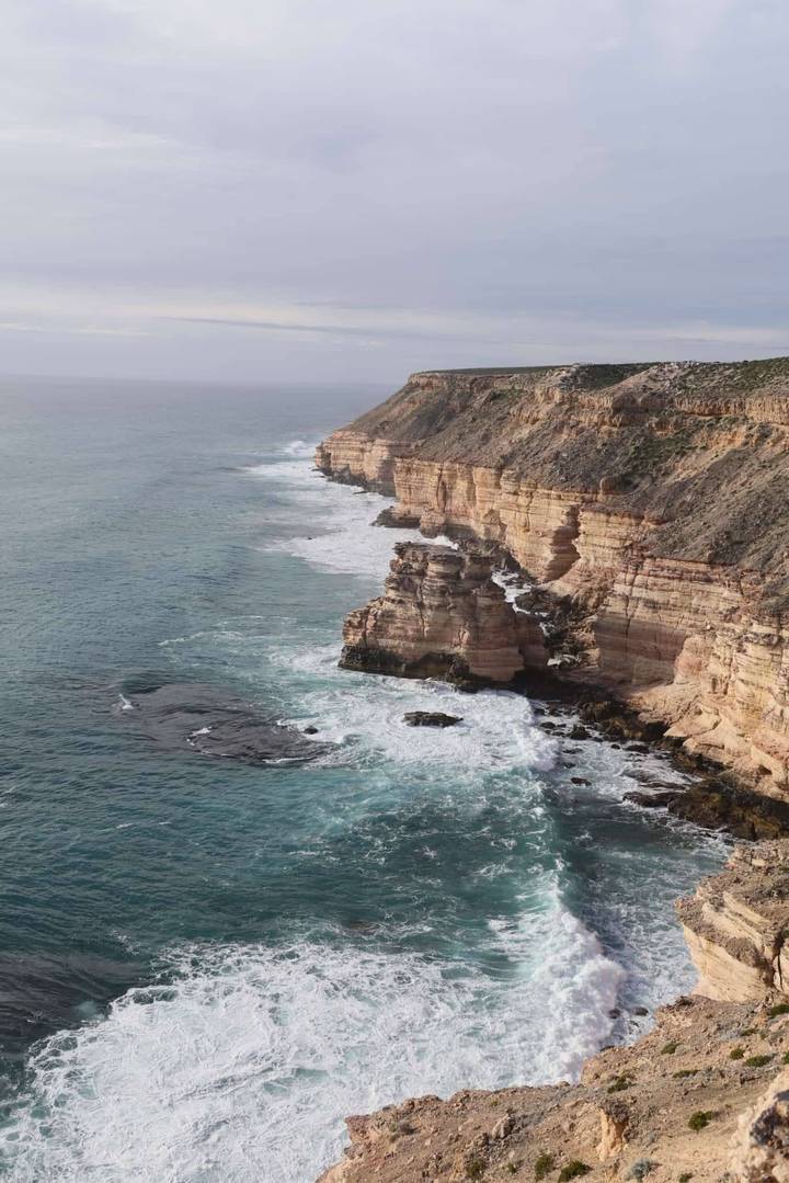 Dramatic coastal cliffs drop to turquoise waves, layers of orange rock reflecting afternoon light.