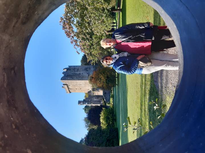 Two women stand in front of Blarney Castle framed by a circular stone opening on a sunny morning.