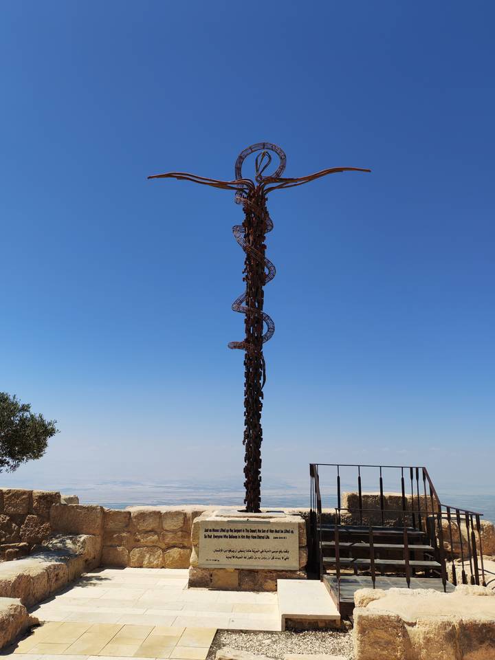 A tall bronze sculpture with spiral serpent motif rises against a clear blue sky.