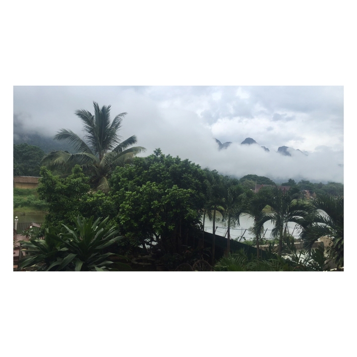 Lush greenery with palm trees and mountains partially shrouded in clouds.
