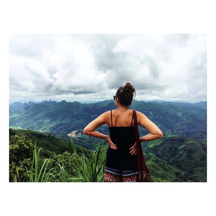 Femme debout, les mains sur les hanches, surplombant un paysage montagneux.