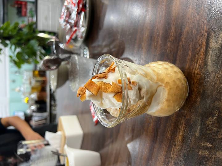Close-up of a creamy Vietnamese dessert topped with toasted coconut flakes in a glass cup.