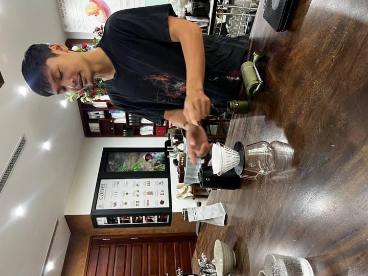 Barista prepares a manual pour-over coffee setup on a wooden countertop.