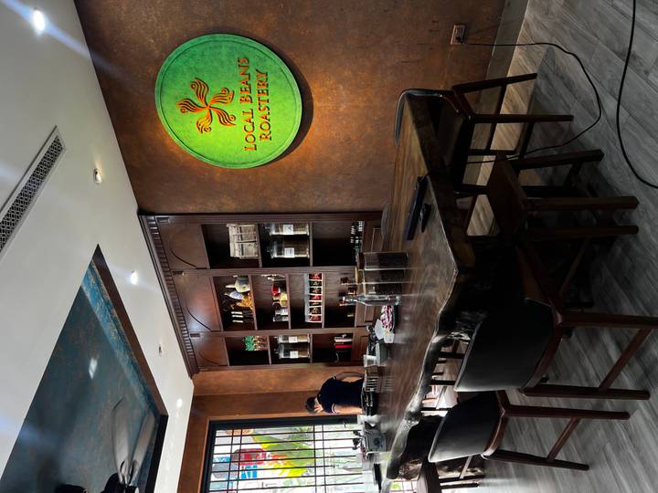 Interior of a boutique coffee roastery featuring wooden shelving, jars of beans, and a lit company logo sign.