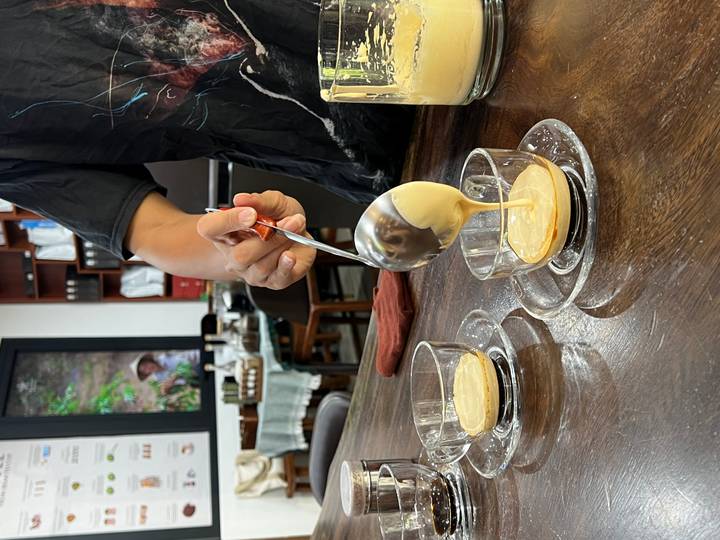Barista ladles creamy egg mixture into cups of Vietnamese coffee during a demonstration.