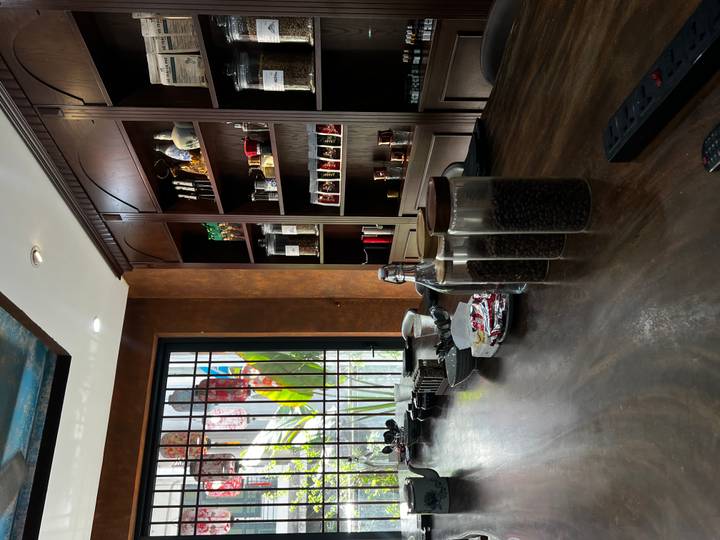 Sunlit corner of a coffee studio with shelves of brewing equipment and jars of beans beside a barred window.