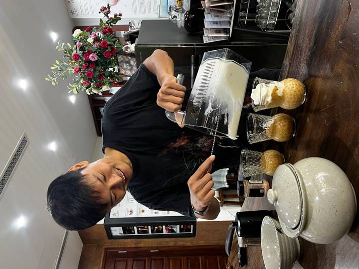 Barista pours creamy topping from a blender into individual glasses of Vietnamese coffee.