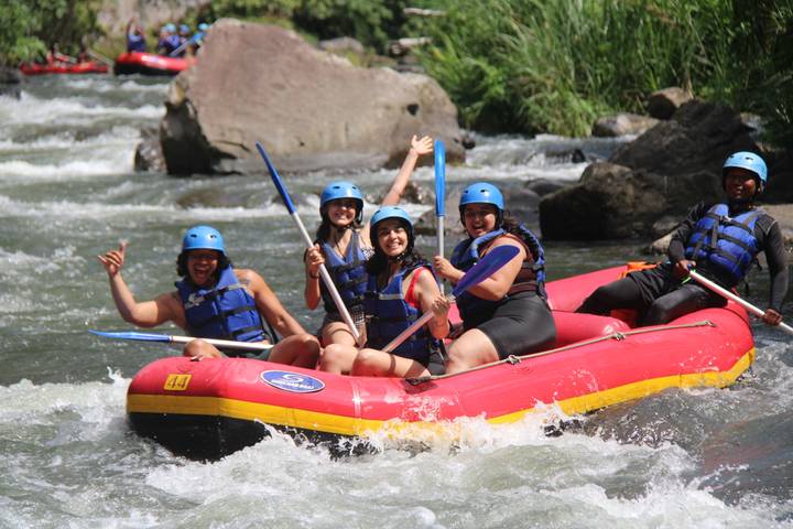 Laughing rafters maneuver a red inflatable boat through white-water rapids in the sunshine.
