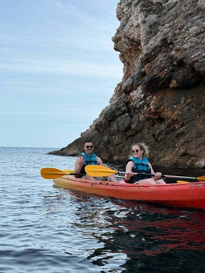 Couple kayaking along rocky Adriatic coastline under soft light.