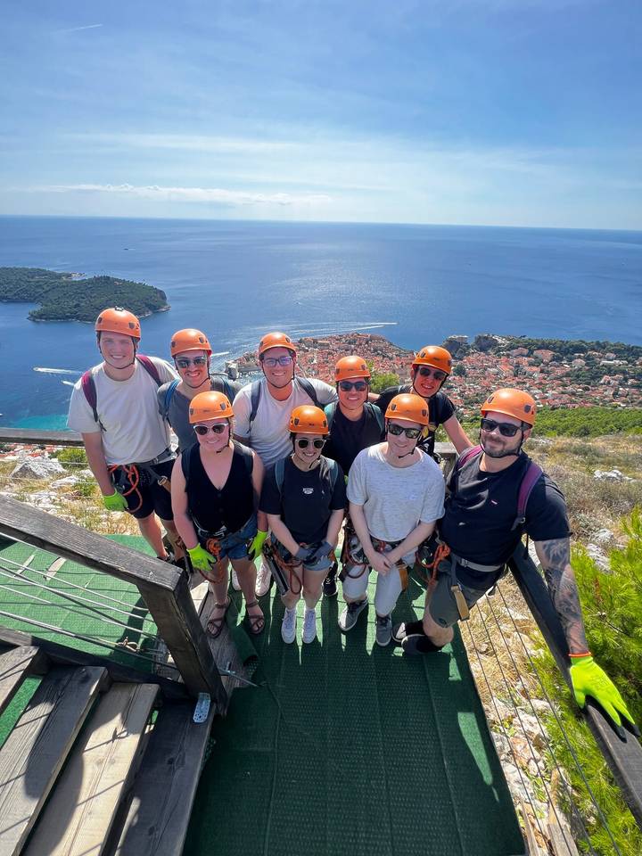 Adventure group in helmets on a cliff-top zipline platform overlooking Dubrovnik and the Adriatic.