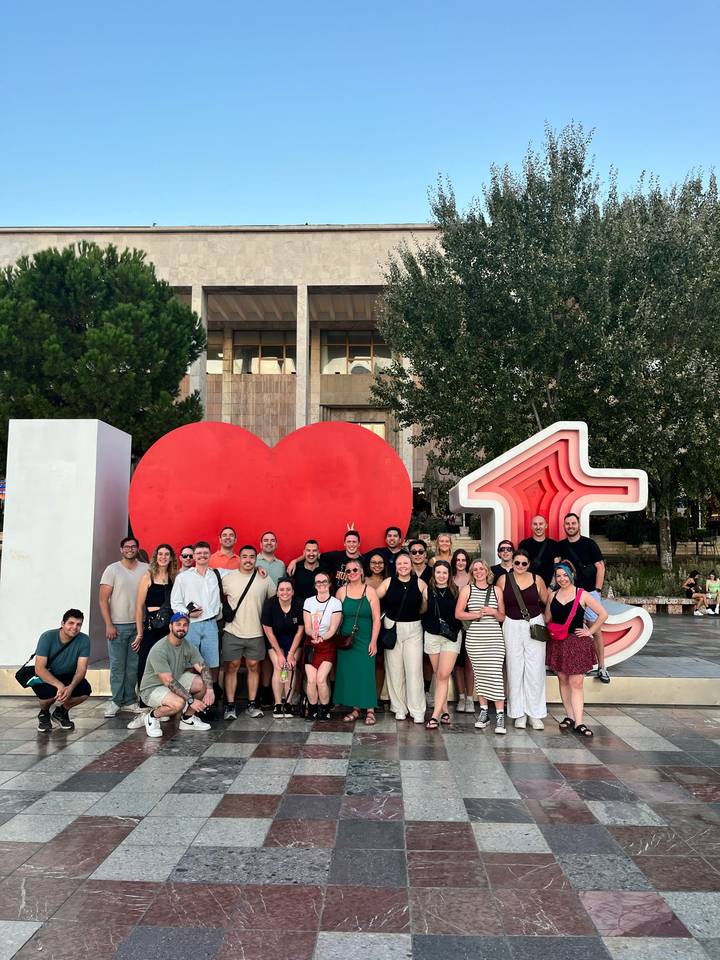 Large travel group posing in front of the red heart sculpture in Tirana city square.
