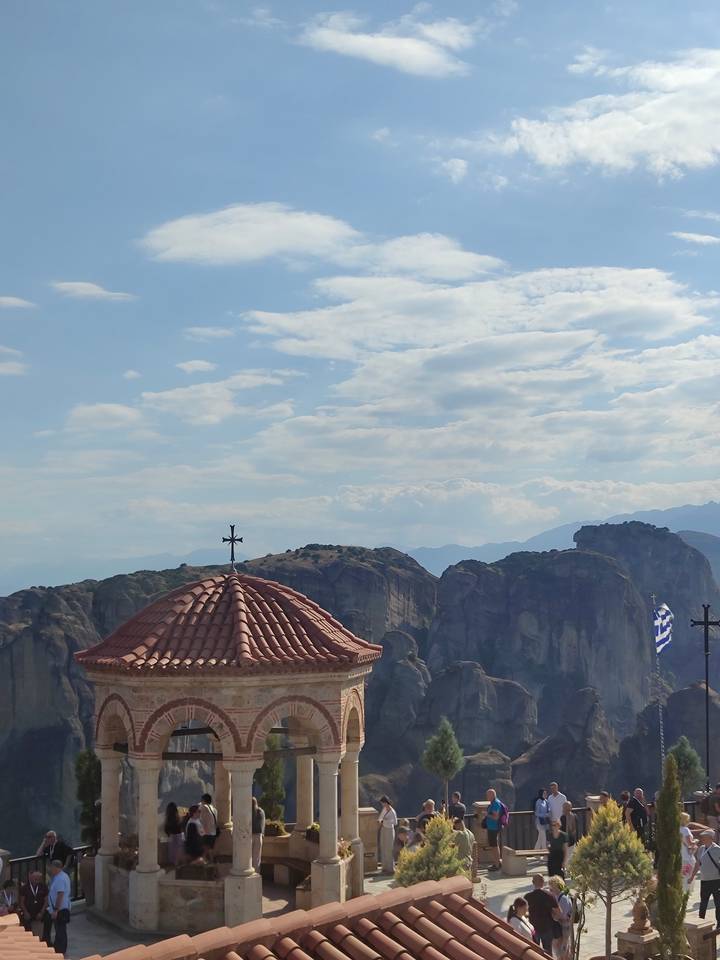 Tiled monastery rooftop and Greek flag with the towering rock pillars of Meteora beyond.