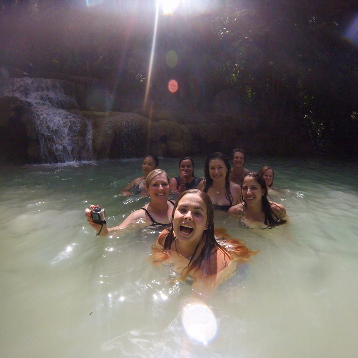 A group of people enjoying a dip in a scenic waterfall pool.
